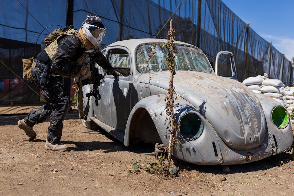 Man in Paintball Gear Hiding behind a Rusty Volkswagen Beetle Car Body